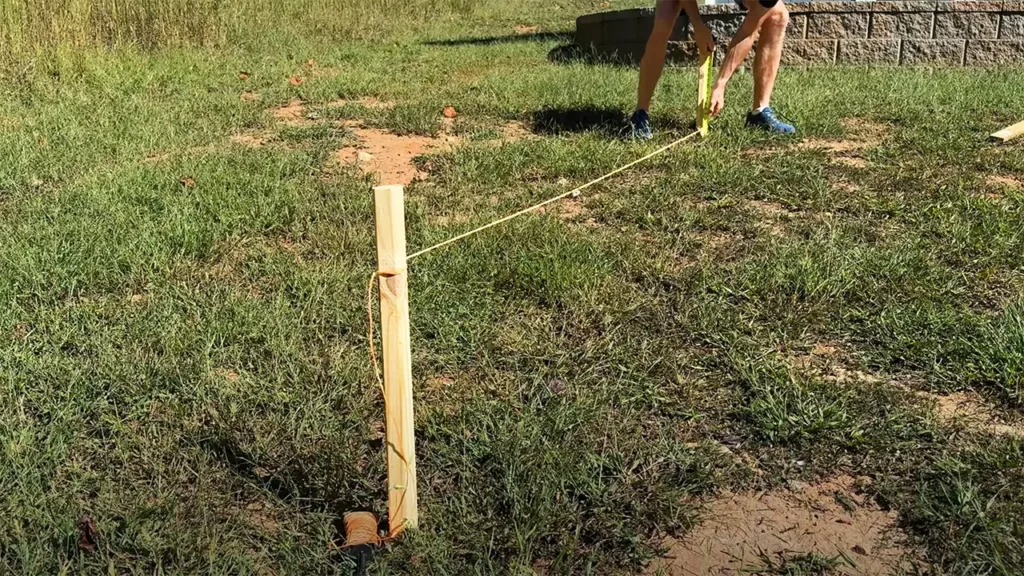 Yard slope being measured using two wooden stakes, string, bubble level and tape measure.